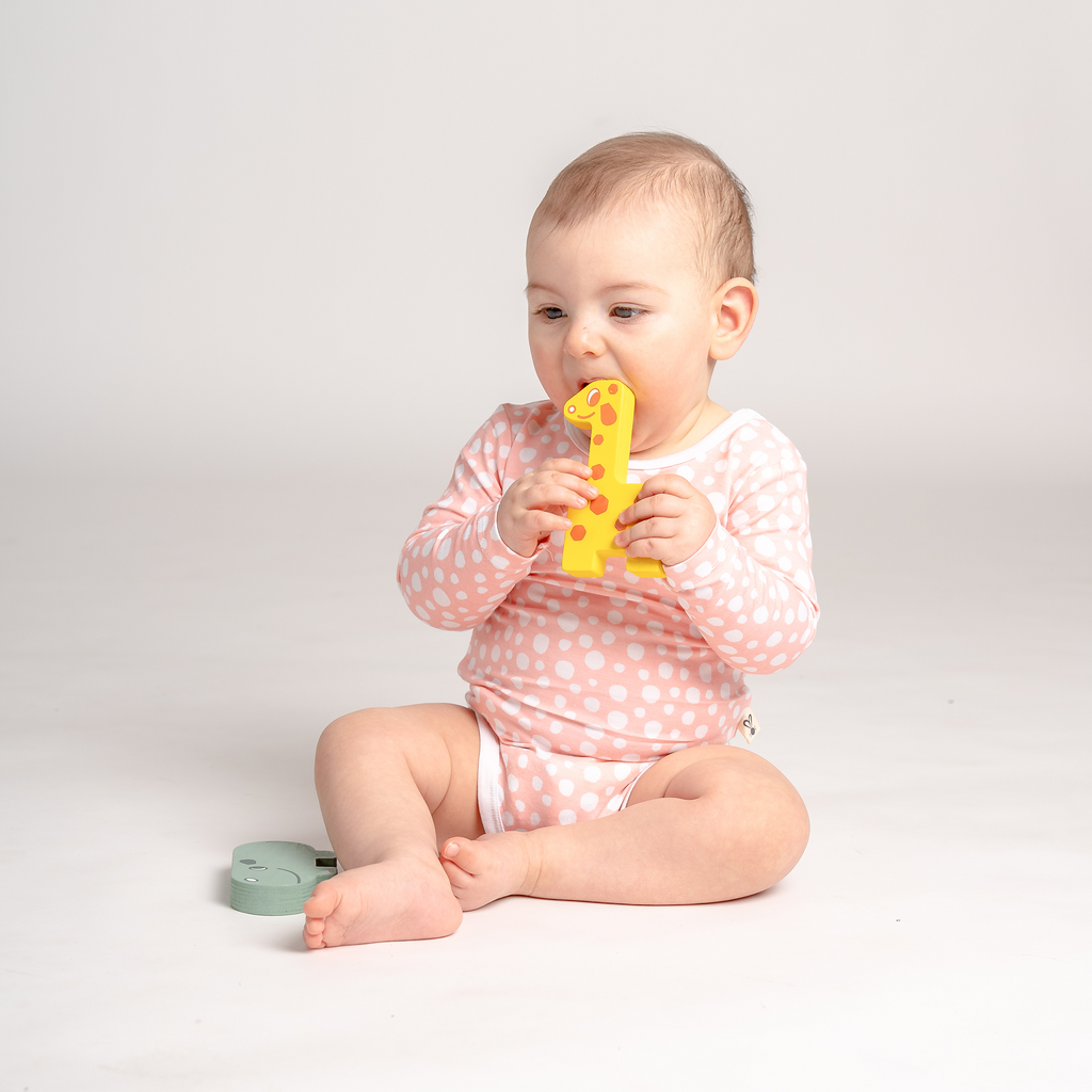 Little baby girl playing in LiaaBébé toddler long sleeve bodysuit in Light Pink color with dots.