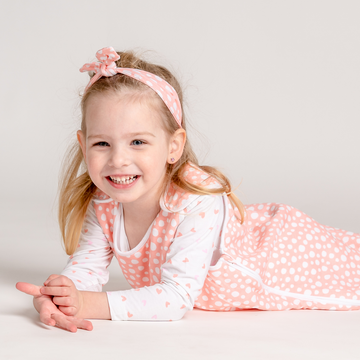 Little baby girl wearing LiaaBébé Top Knot Headband in light pink color with dots.