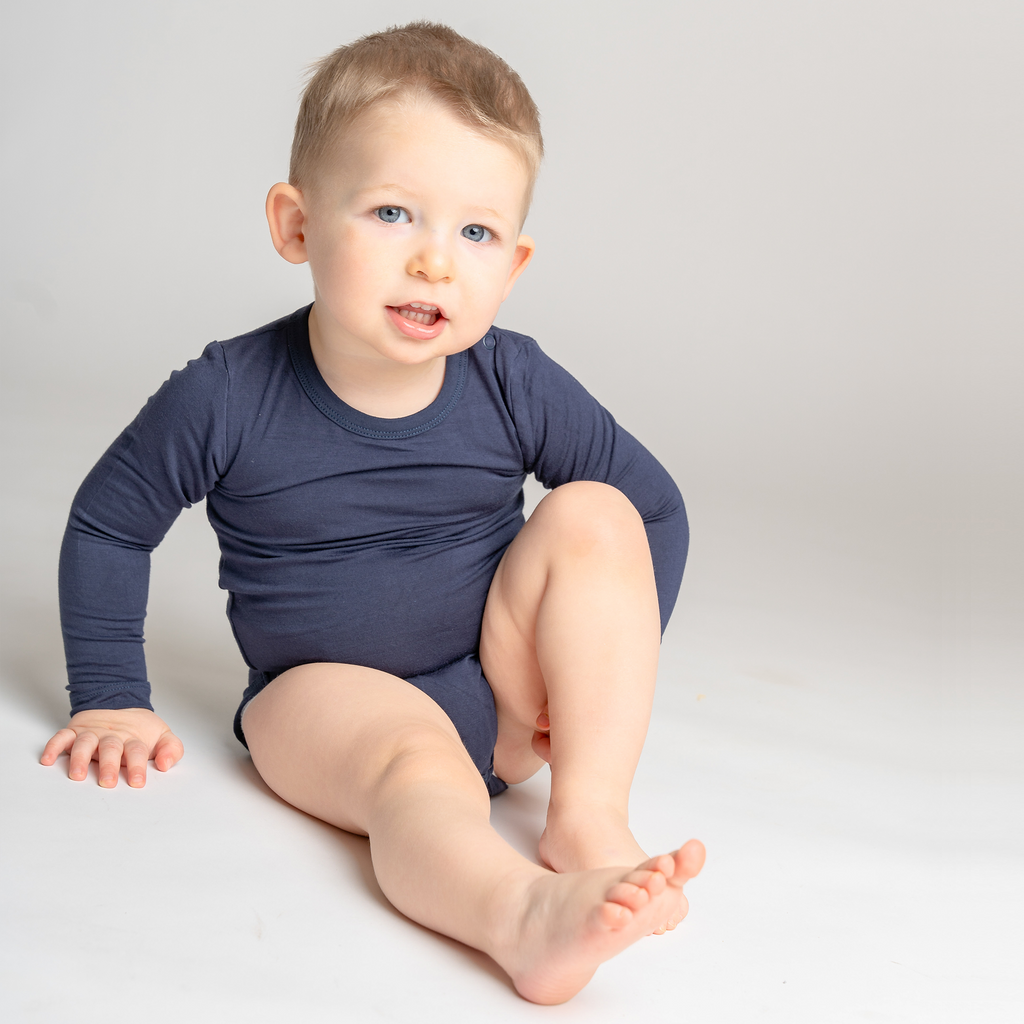 Smiling little boy wearing LiaaBébé Long Sleeve Bodysuit in navy blue color.