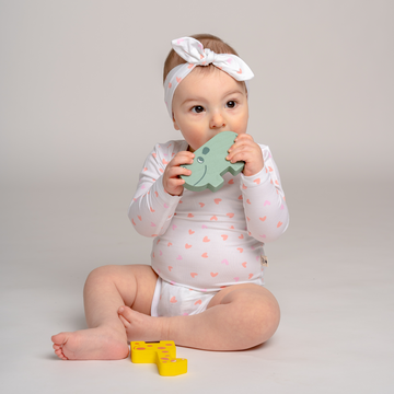 Little baby girl playing and wearing toddler LiaaBébé bodysuit with hearts and also matching headband.